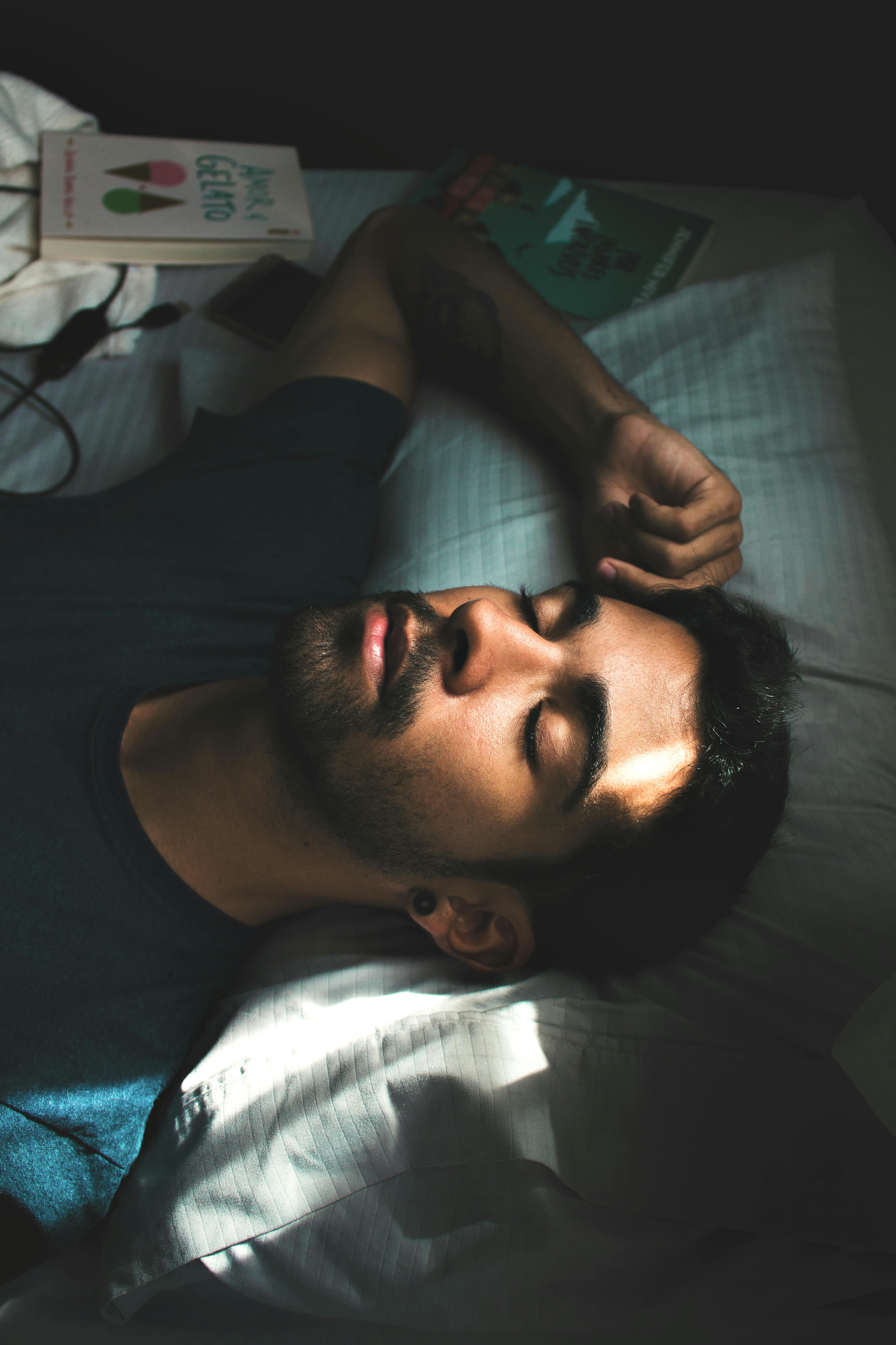 A man with black hair and a black shirt lies in a bed sleeping